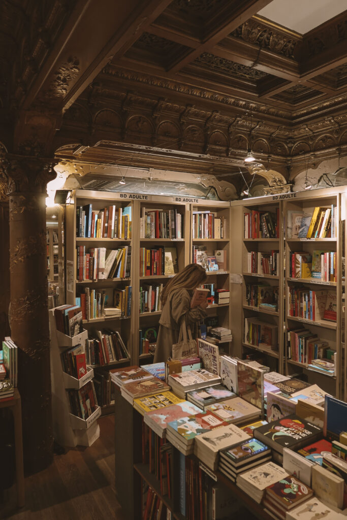 A young woman reading a book in an opulent bookstore interior featuring grand mirrors and intricate golden stucco ceilings
