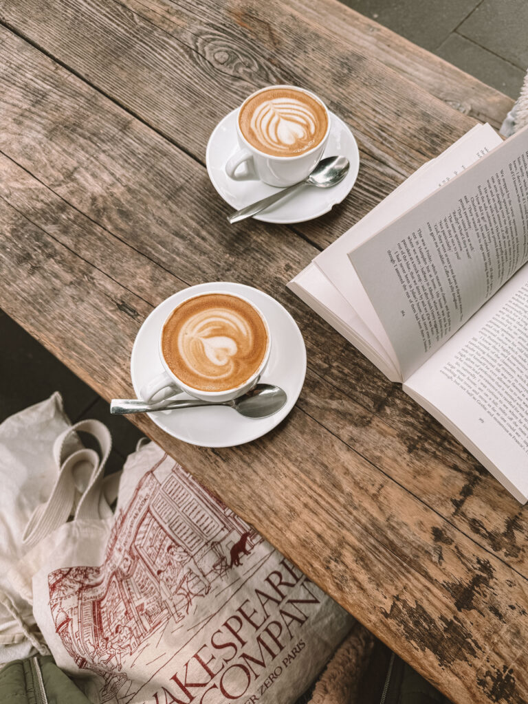 offenes Buch neben einer Tasse Kaffee auf einem Cafétisch