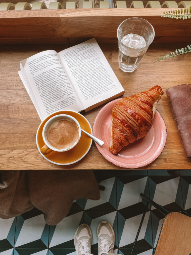 Roman und Cappuccino auf einem kleinen Holztisch im Café mit Croissant